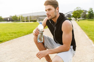 Kulak egzersizi yaparken su içen erkeksi bir adam.