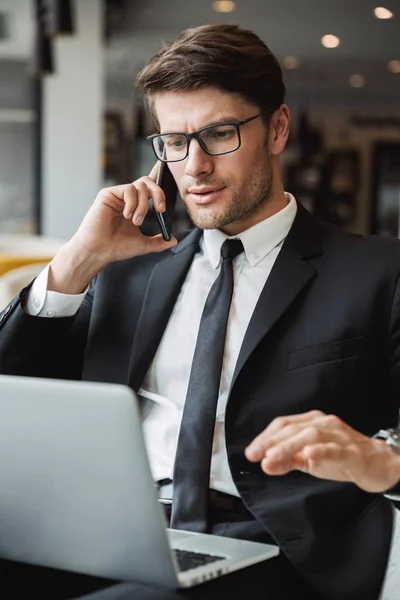 Kuva komea liikemies käyttää kannettavaa tietokonetta ja puhuu — kuvapankkivalokuva