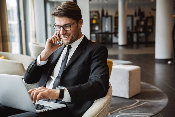 Foto de joven empresario feliz usando ordenador portátil y talki —  Fotos de Stock