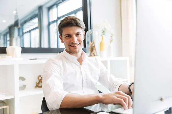 Image of smiling businesslike man sitting at table and working on computer in office — Stock Photo, Image