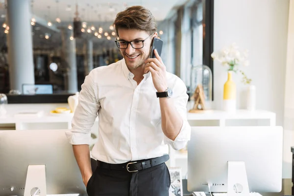 Image of attractive businesslike man talking on cellphone while working in office — Stock Photo, Image
