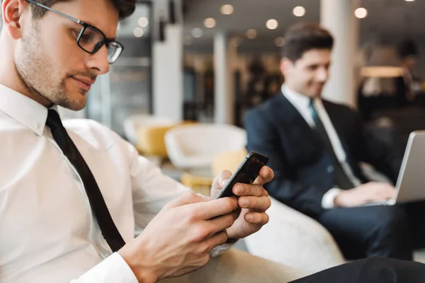 Confrères hommes d'affaires concentrés à l'intérieur dans le bureau du centre d'affaires en utilisant un téléphone mobile et un ordinateur portable . — Photo