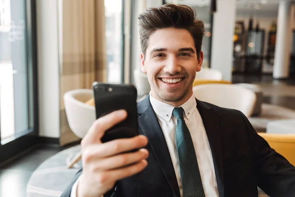 Happy cheery businessman indoors in business center office using mobile phone. — Stock Photo, Image