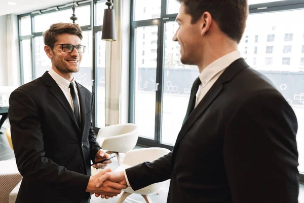 Colleagues indoors in business center office using mobile phone shaking hands. — Stock Photo, Image