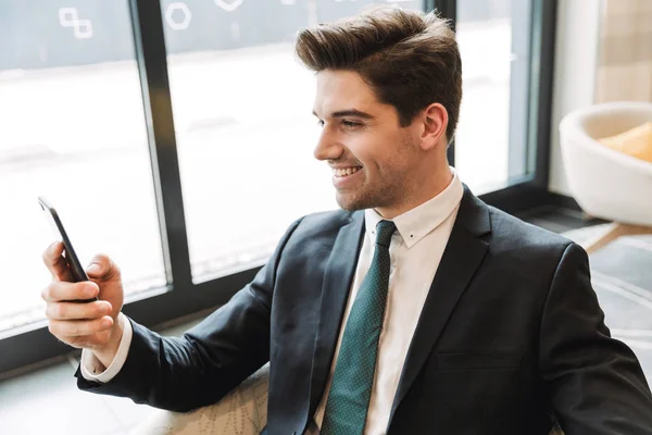 Happy cheery businessman indoors in business center office using mobile phone. — Stock Photo, Image