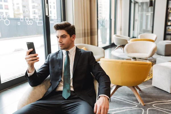 Young serious businessman indoors in business center office using mobile phone. — Stock Photo, Image