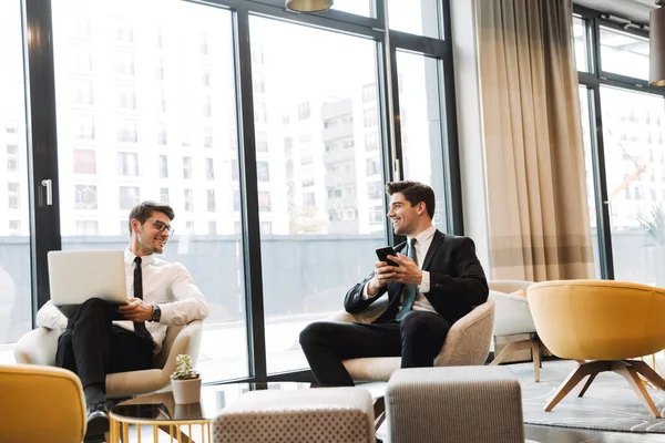 Улыбаясь позитивным бизнесменам, коллеги в помещении офиса бизнес-центра используют мобильный телефон и ноутбук . — стоковое фото