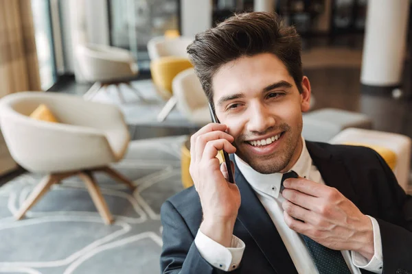 Optimistic cheery businessman indoors in business center office talking by mobile phone. — Stock Photo, Image