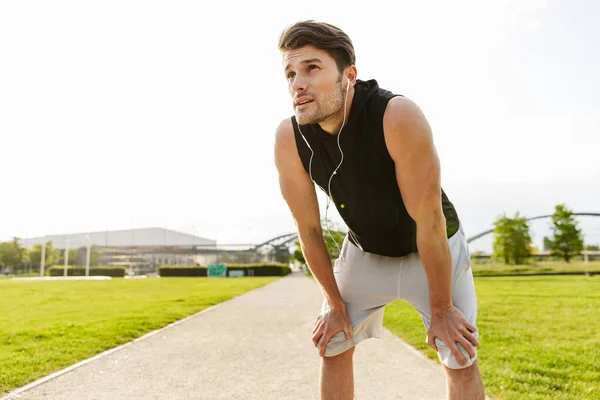 Foto di un uomo concentrato che si allena con le cuffie e corre al parco verde all'aperto al mattino — Foto Stock