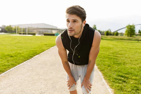 Photo of concentrated man working out with earphones and running at green park outdoors in morning — Stock Photo, Image