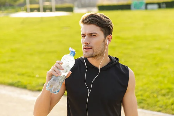 이어폰을 가지고 놀다가 야외 야외 야외에서 뛰고 있는 남성 이 물을 마시고 있는 모습 — 스톡 사진
