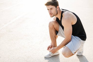 Spor ayakkabı bağcıklarını bağlayan yakışıklı bir adam resmi.