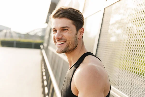 Fotografie pozitivního mladého muže, který se usmívá, když stojí na sportovní gro — Stock fotografie