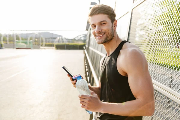 그린 파크에서 아침 운동하는 동안 스포츠 경기장에서 서 핸드폰을 들고 있는 행복 한 남자의 사진 — 스톡 사진