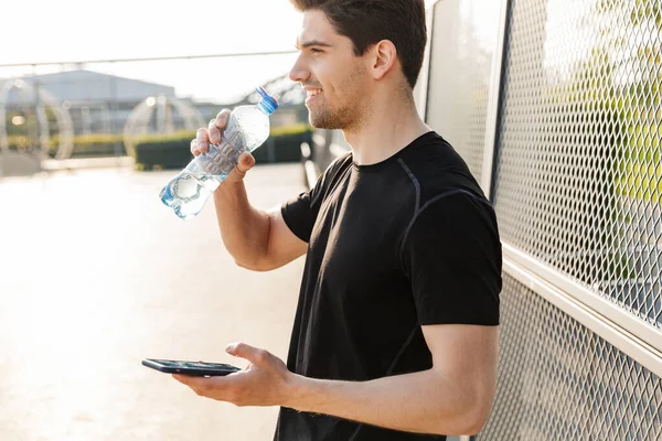 Portré vidám ember kezében mobiltelefon és vizes palack, miközben — Stock Fotó