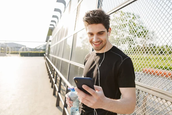 Πορτραίτο του ελκυστικού άνδρα κρατώντας κινητό τηλέφωνο και μπουκάλι νερό — Φωτογραφία Αρχείου