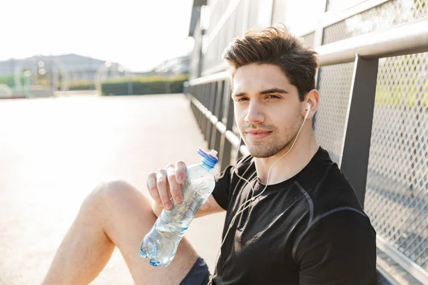 Egy aktív férfi arcképe, aki fülhallgatót visel, és vizes palackot tart. — Stock Fotó
