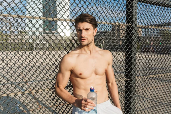 Porträt eines maskulinen, hemdlosen Sportlers mit Wasserflasche — Stockfoto