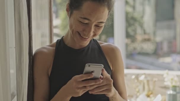 Feliz Mujer Asiática Bonita Pie Cerca Ventana Uso Teléfono Inteligente — Vídeo de stock