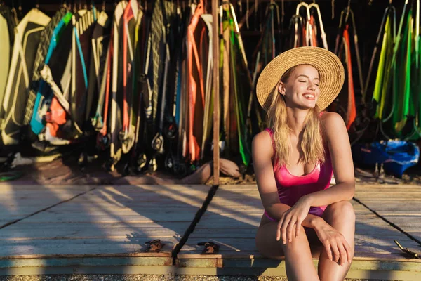 Imagem de mulher branca sorridente sentada perto de pranchas de surf e velas — Fotografia de Stock