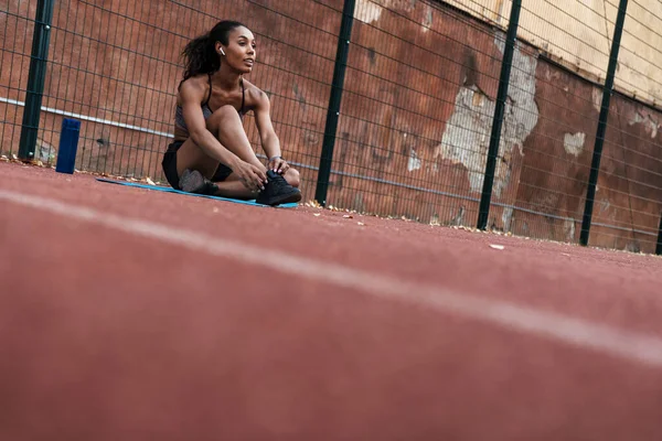 Image of african american woman with earbuds sitting at playgrou — Stock Photo, Image