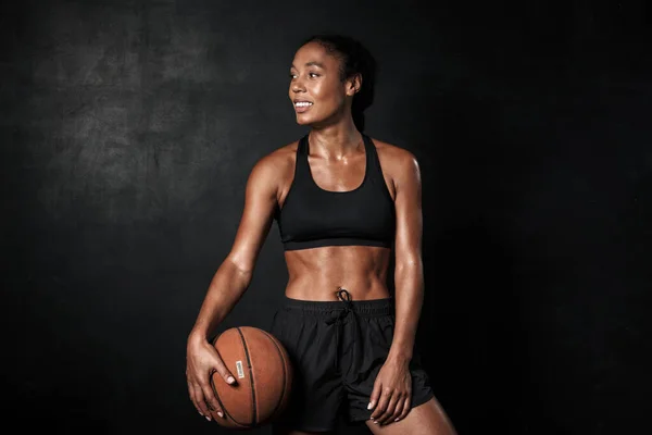 Imagen de la sonriente mujer afroamericana en ropa deportiva sosteniendo baloncesto — Foto de Stock