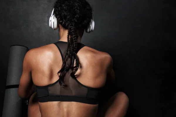 Εικόνα μιας νεαρής Αφροαμερικανής γυναίκας με αθλητικά ρούχα που κάθεται με ακουστικά — Φωτογραφία Αρχείου