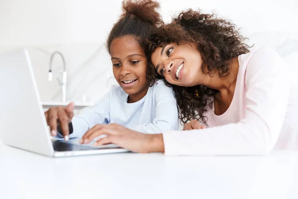 Image of african american woman and her daughter using laptop at