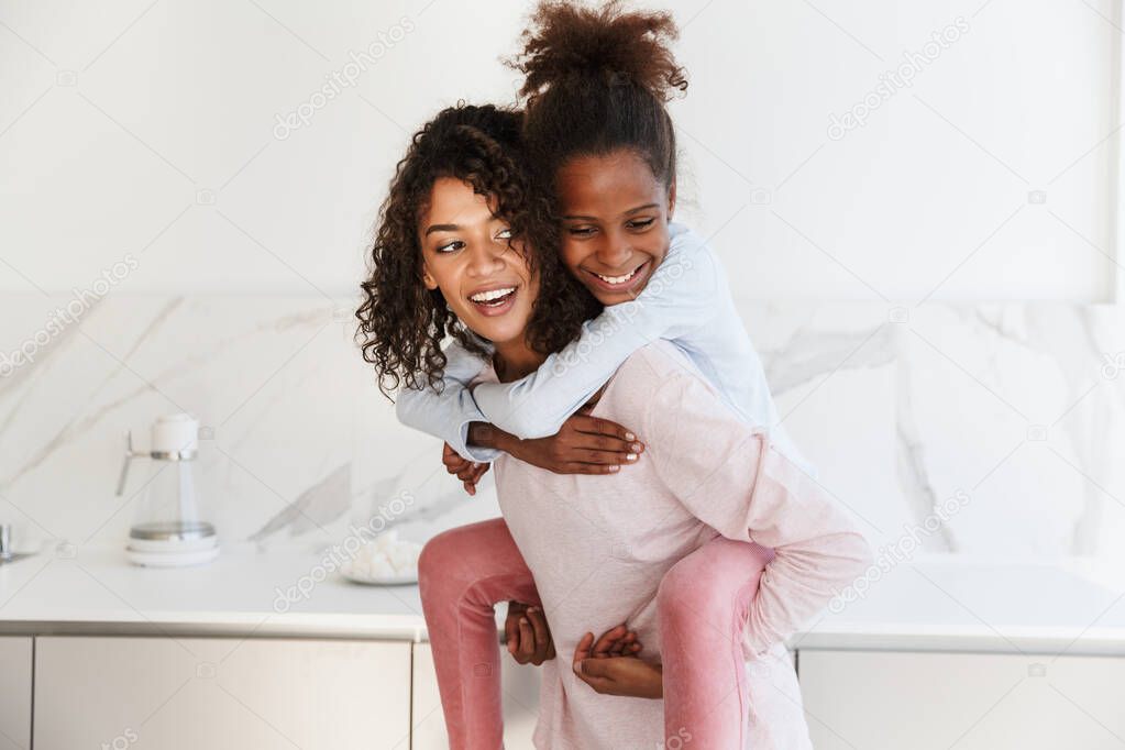 Image of african american woman piggybacking her daughter at hom