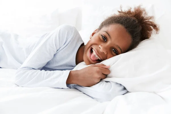 Изображение африканской американской маленькой девочки, улыбающейся и лежащей в постели — стоковое фото