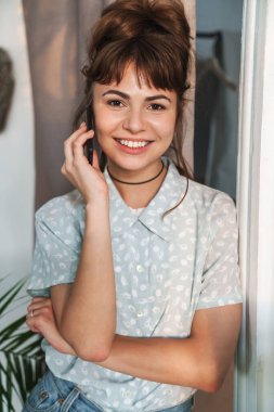 Neşeli, mutlu, mutlu, güzel bir kadın cep telefonuyla evde konuşuyor..