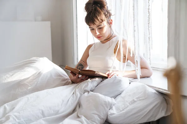 Güzel bayan evde, evde kitap okurken yatakta uzanıyor.. — Stok fotoğraf