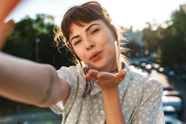Genç, neşeli, pozitif, balkonda güzel bir kadın öpücüklerle selfie çekiyor..