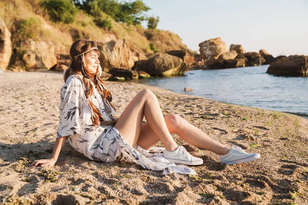 Image of gorgeous hippy girl in feather headband sitting by seas — Stock Photo, Image
