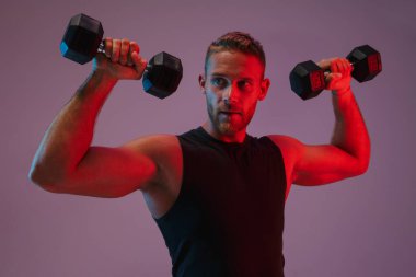 Konsantre olmuş genç sporcu, dambıllarla egzersiz yapıyor..