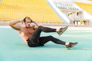 Yeşil spor sahasında yatan ve çapraz çizim yapan bir adam. 