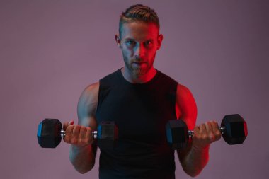 Konsantre olmuş genç sporcu, dambıllarla egzersiz yapıyor..