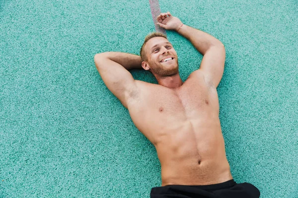 Image of happy shirtless man lying at green sports ground outdoo — Stockfoto