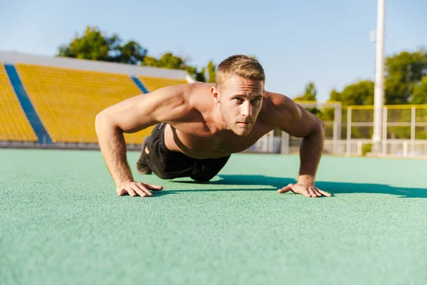 Bild eines aktiven, hemdslosen Mannes, der Liegestütze auf dem Sportplatz macht — Stockfoto