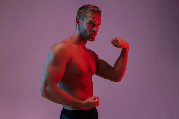 Jaki sport lubisz najbardziej? man posing isolated over neon lights showing biceps. — Zdjęcie stockowe