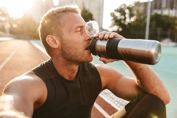Imagem do desportista muscular a beber água no estádio ao ar livre — Fotografia de Stock