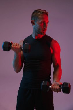 Konsantre olmuş genç sporcu, dambıllarla egzersiz yapıyor..