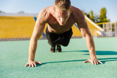 Spor sahasında şınav çeken atletik tişörtsüz bir adam. 