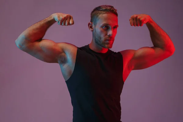 Ung idrottsman poserar isolerad visar biceps över neon ljus. — Stockfoto