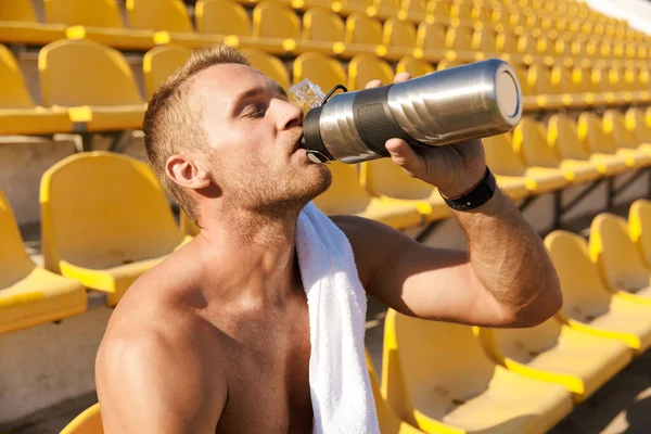 Kép fiatal félmeztelen sportoló ivóvíz a stadionban tenger — Stock Fotó