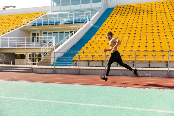 Imagen de deportista sin camisa corriendo en pista contra estadio se — Foto de Stock