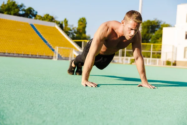 Obrázek svalnatého muže bez trička, jak dělá kliky na sportovním hřišti — Stock fotografie