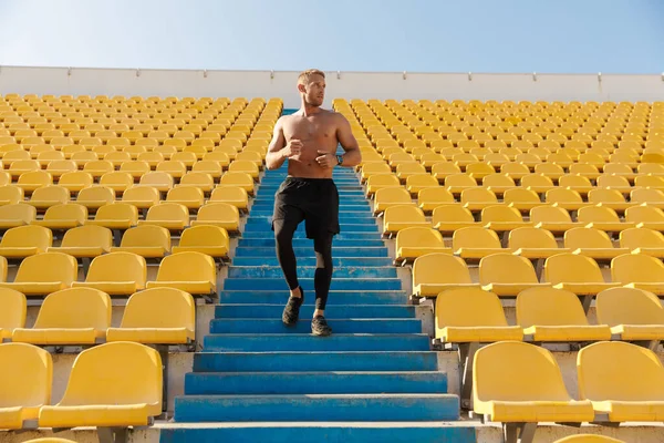 Imagen del deportista caucásico corriendo por los asientos del estadio mientras hace — Foto de Stock