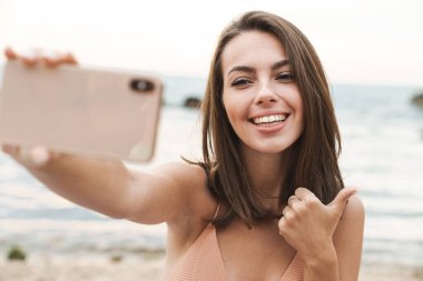Başparmağını gösteren ve cep telefonuyla selfie çeken bir kadın resmi.