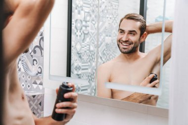 Gülümseyen genç üstsüz adam deodorant sürüyor.